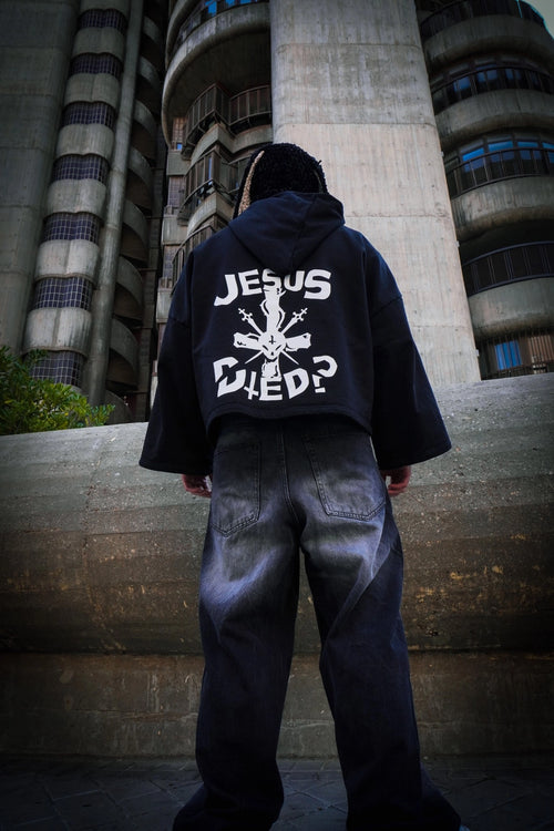 Persona de espaldas con sudadera “Jesus Died?” en un entorno urbano y industrial