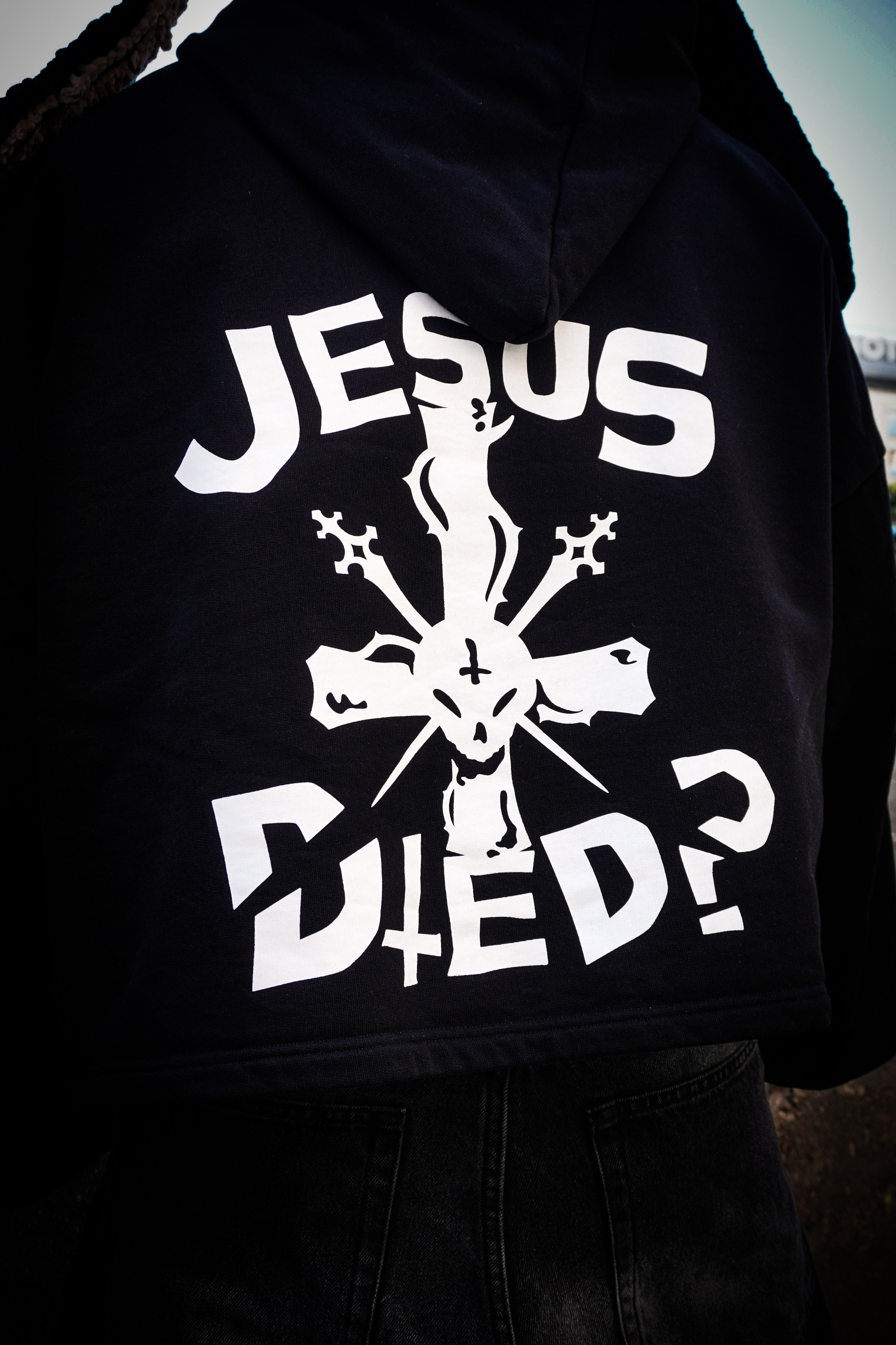 Primer plano del estampado “Jesus Died?” en la parte trasera de una sudadera negra